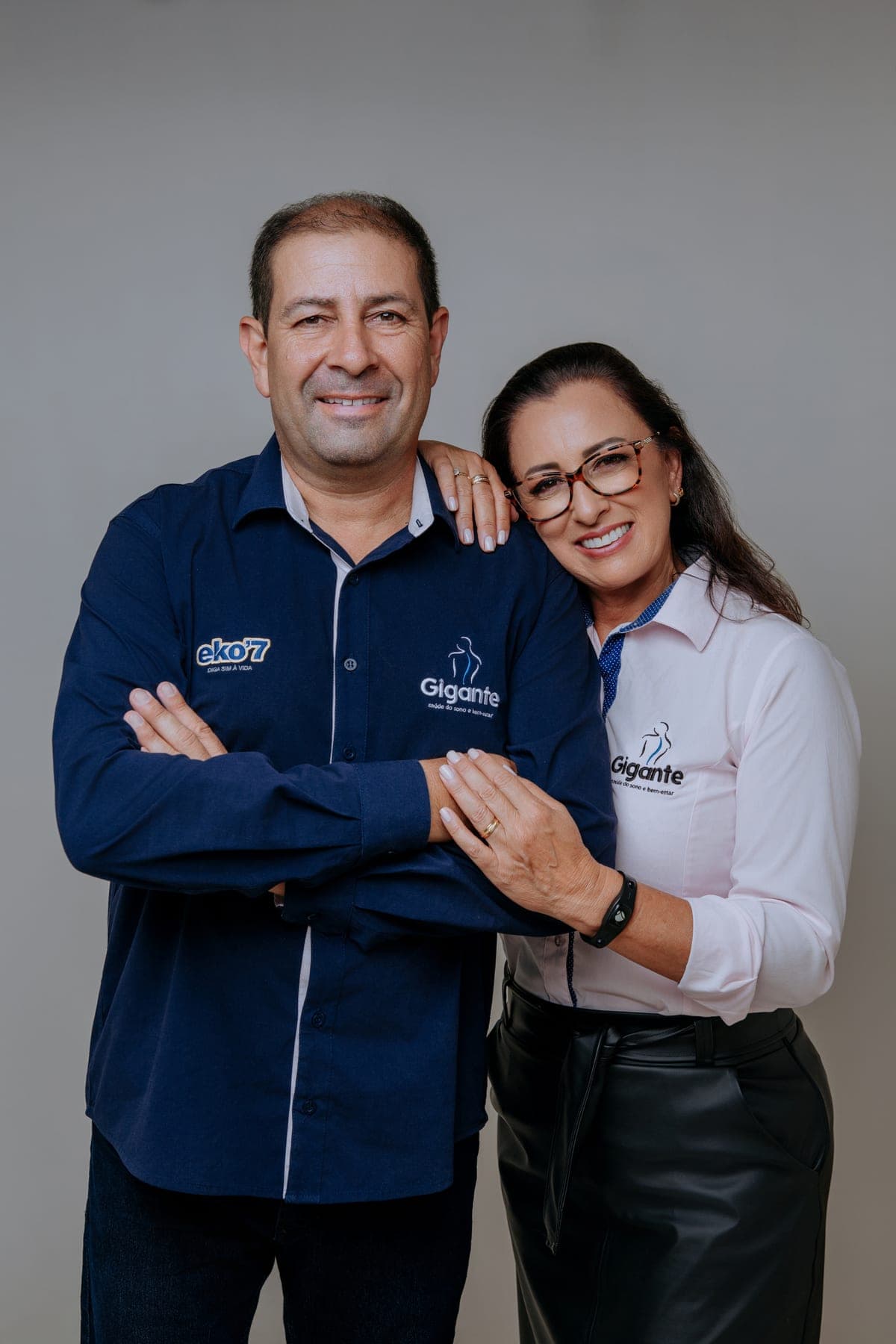 Silvana e Carlinhos, fundadores da Gigante Saúde do Sono, abraçados e sorrindo com o uniforme da marca